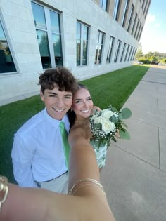 a man and woman taking a selfie in front of a building with green grass