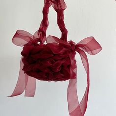 a red purse hanging from a hook on a white wall with ribbon around the handle