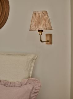 a lamp is on the wall next to a bed with a pink comforter and pillow