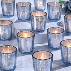 many blue glass candles are lined up on a white table with silver and gold flecks