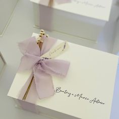 two white boxes with purple ribbons on them and some writing on the inside of each box