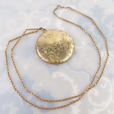 An elaborate engraved foliate design tops this large 1 5/8-inch round Antique gold filled locket. The design was finely carved with flowers, leaves, scrolled lines, a fine straight line sun ray pattern and has a blank area meant for a monogram. The back has a plain shiny gold finish.  The locket opens with a small fingernail groove at the top and closes lightly, but securely. The inside has no frames or inserts, just an old black and white photograph. One side is signed, "D&C" and the locket tested as gold filled (no hallmark). The large pendant hangs from a thick, well-made sturdy vintage gold filled curb chain. It has a nice sheen and true vintage look. The chain stretches 23 1/2 inches and has no clasp. It must be put over the head to wear, so it may not fit everyone. This pairing is in Gold Medallion Locket Necklace Stamped 14k, Victorian Round Locket Necklace Stamped 14k, Antique Medallion Locket Necklace Stamped 14k, Gold Medallion Locket Necklace In Brass, Gold Brass Round Pendant Locket Necklace, Gold Brass Locket Necklace With Round Pendant, Engraved Rose Gold Round Pendant Locket Necklace, Engraved Rose Gold Locket Necklace With Round Pendant, Antique Yellow Gold Medallion Locket Necklace