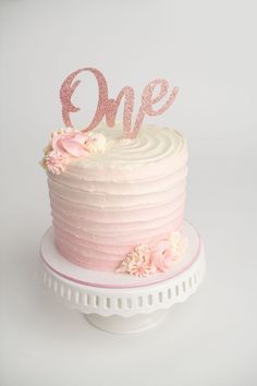 a pink cake with white frosting and flowers on the top that says'one '