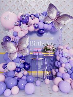 a birthday party with purple balloons and butterflies on the wall, cake table and decorations