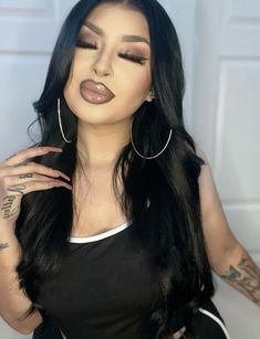 a woman with long black hair wearing large hoop earrings and tattoos on her left arm