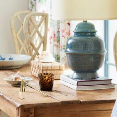 a wooden table topped with a blue vase next to a lamp and plate on top of it