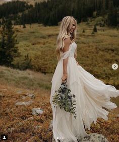 a woman in a white dress is walking through the grass with her long flowing skirt