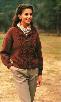 a woman wearing a red sweater and tan pants standing in front of a field with trees