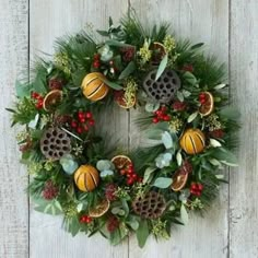 a wreath with oranges, berries and pine cones hanging on a white wooden wall