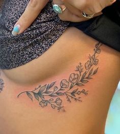 a woman's lower back tattoo with flowers and leaves on her stomach, showing the side