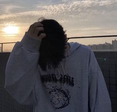 a person with long hair standing in front of a fence and looking at the sky