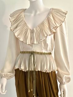 "STUNNING vintage C1970s high end, off white or ivory sumptuous long sleeve silk blouse by Partique, featuring a lavish V neck collar with pleated ruffles fully edged in gold trim, a peplum hem, also with pleated ruffles fully edged in gold trim, and a three button front closure. Channeling Old Hollywood elegance and glamour, this rare beauty is a guaranteed head turner! Approximate Measurements: Chest: 38\"; Shoulder: 16\"; Waist: 27\"; Length: 19 1/2\" Labeled a Size 6 Please Note: Partique bl Long Sleeve Cream Blouse For Wedding, Spring Evening Cream Blouse, Cream Long Sleeve Blouse For Evening, Beige Long Sleeve Blouse For Evening, Elegant Long Sleeve Tops For Vintage Fashion, Retro Long Sleeve Blouse For Evening, Classic Cream Party Blouse, Retro Long Sleeve Evening Blouse, Vintage Beige Blouse For Spring