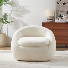 a white chair sitting on top of a rug next to a dresser and potted plant