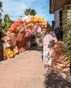 an archway made out of balloons and other decorations on the side of a road with palm trees