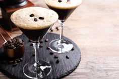 two glasses filled with chocolate pudding on top of a wooden table next to coffee beans