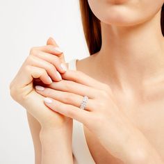 a woman wearing a diamond ring and white dress holding her hand up to her chest