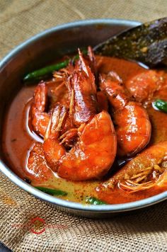 a metal bowl filled with shrimp and sauce on top of a cloth covered tablecloth