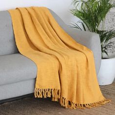 a couch with a yellow blanket on top of it next to a potted plant