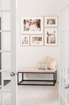 a white bench sitting in front of pictures on the wall next to a doorway with an open door