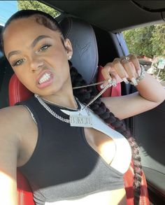 a woman sitting in the back seat of a car with chains on her necklaces