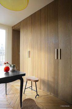 a room with a table, chair and vase on top of it in front of a wooden paneled wall