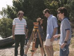 three men standing next to each other in front of a wooden tripod with a camera on it