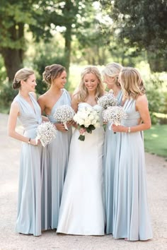 a group of women standing next to each other in front of trees and grass with bouquets