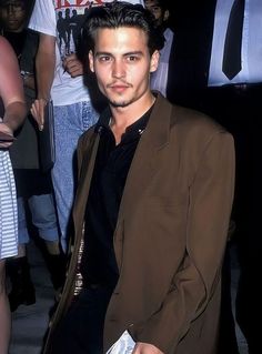 a man in a brown jacket and black shirt is standing near other people at an event