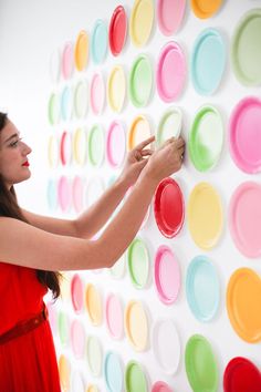 a woman in a red dress is painting on a wall with plates and paintbrushes