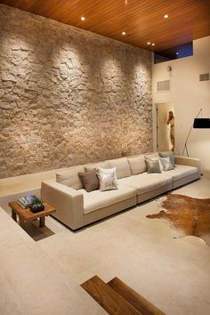 a modern living room with stone walls and wood ceilinging, large sectional couch in the center