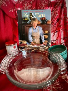 there is a glass pie dish and cookbook on the table with red cloths