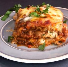 a white plate topped with lasagna covered in sauce and cheese, garnished with parsley