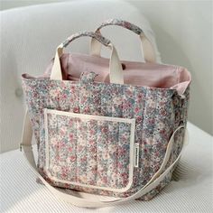 a floral bag sitting on top of a white couch next to a pink and blue purse