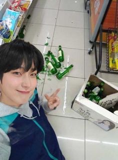 a young man sitting on the floor in front of a pile of soda bottles with his finger up