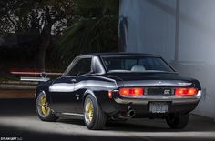 a black car parked in front of a white building with yellow rims on it's tires