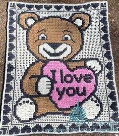 a crocheted teddy bear holding a heart with the words i love you written on it