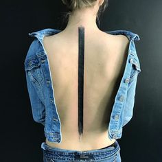 the back of a woman's jean jacket with a tattoo on her lower back