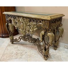 an ornate console table with glass top and gold leaf decorations on the legs, in a living room