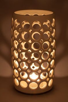 a lit up candle holder with circles and holes on the side, in front of a brown background