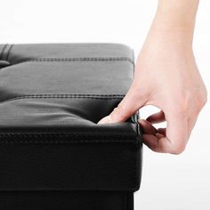 a person's hand is pulling up the top of a black leather ottoman