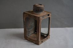 an old, rusty lantern is sitting on a white surface with a gray wall in the background