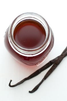 a glass jar filled with liquid sitting on top of a white table next to an unpeeled vanilla