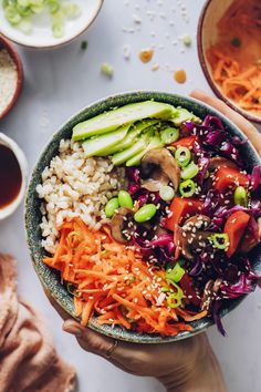 someone holding a bowl filled with vegetables and rice