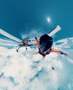 two people are sky diving in the clouds and one person is holding on to his helmet