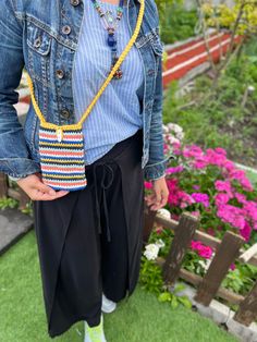 a woman standing in front of flowers wearing a blue jean jacket and black wide legged pants