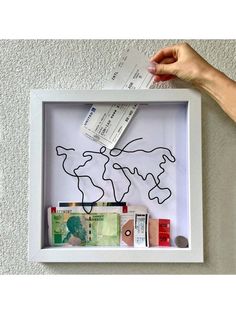 a hand holding a piece of paper in front of a shadow box with money and tickets