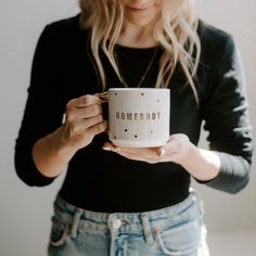 a woman holding a coffee mug with the words homeboy on it in front of her