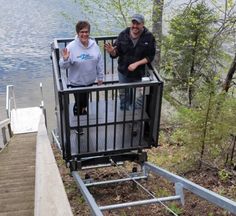 two people standing on top of a metal railing next to a body of water with trees in the background