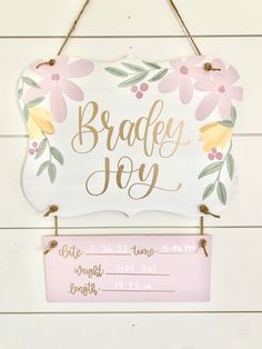 a wooden sign hanging on the side of a white wall with pink and yellow flowers