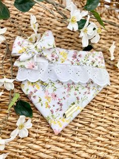 a white dog bandana with flowers and lace on it sitting in front of some branches